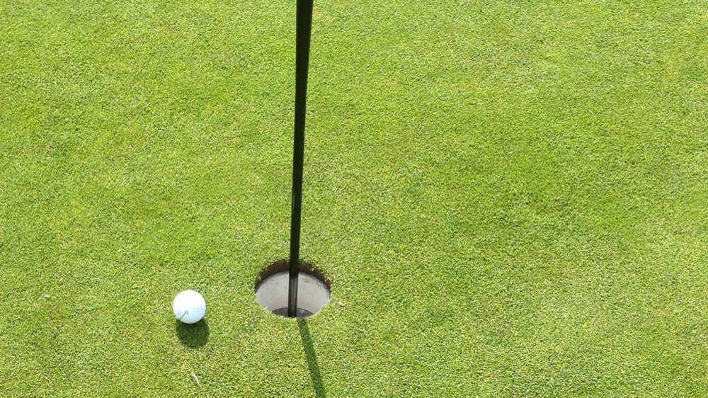 Golf ball resting beside the cup on a putting green